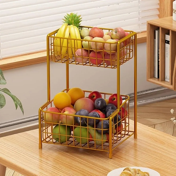 Two-tier metal fruit basket with fruits on a wooden surface.