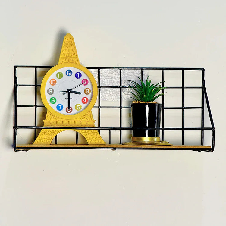 Yellow clock shaped like a ice cream cone on a black metal shelf with a plant against a light background