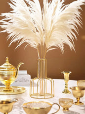 Decorative table setting with gold teapot, candle holders, and a vase with white feathers on a brown background.