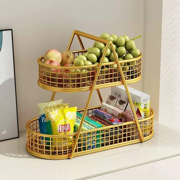 Gold two-tiered basket with apples, snacks, and magazines on a white surface.