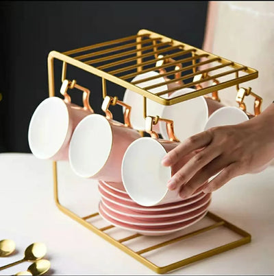 Gold dish drying rack with pink cups and gold spoons on a white surface.