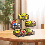 Three-tiered metal fruit basket with fruits and snacks on a wooden table.