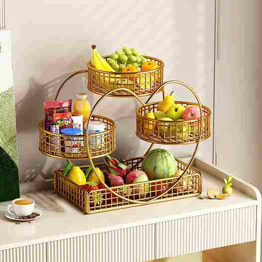 Three-tiered gold wire fruit basket with fruits on a white surface