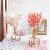 Decorative items including pink dried flowers and feathers in gold vases on a white surface.
