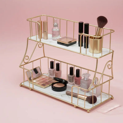 Gold two-tiered makeup organizer with various cosmetic items on a pink background